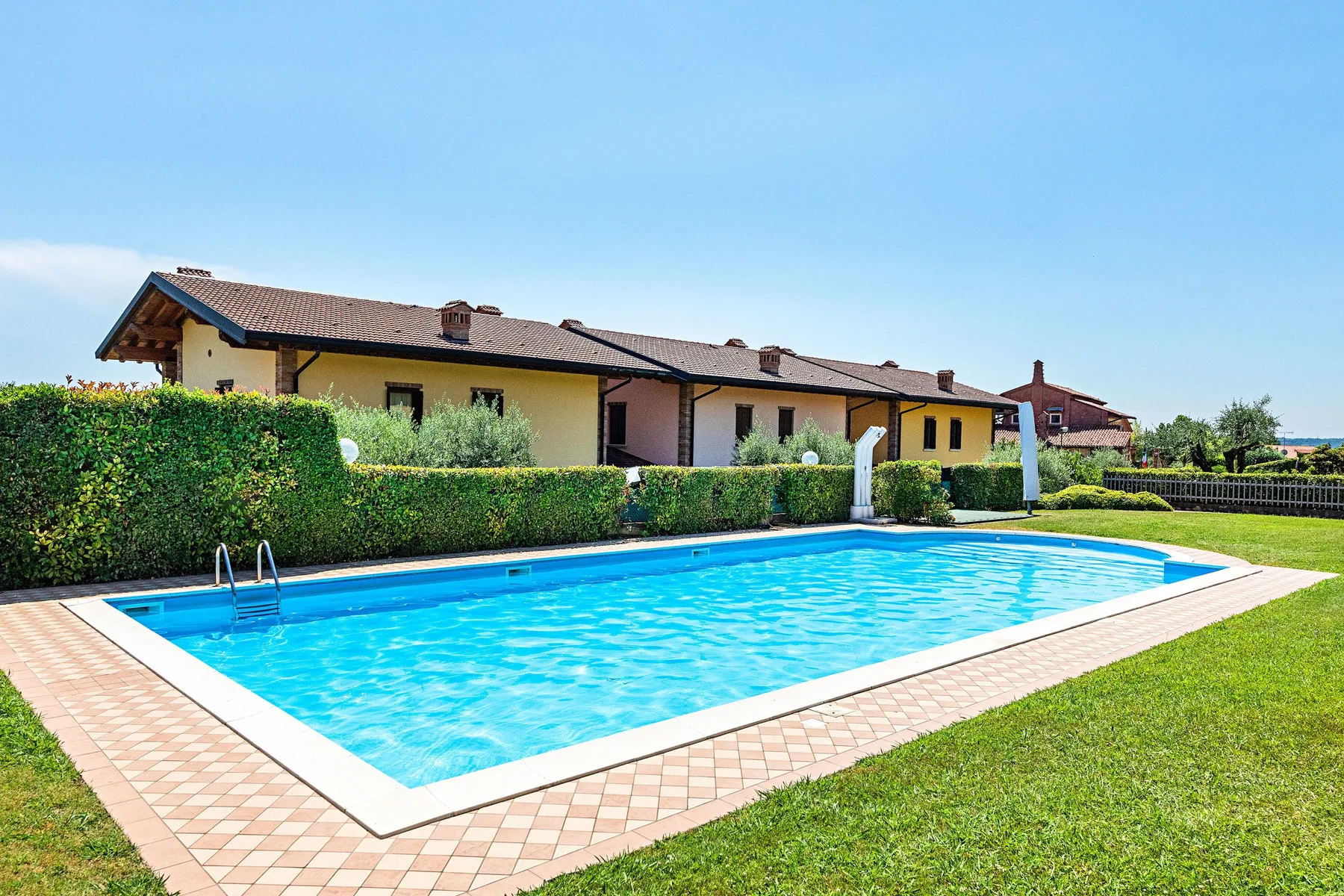 An outdoor swimming pool sits beside a lawn and low residential buildings.