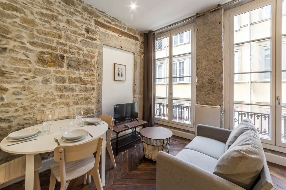 Una sala de estar y comedor con sofá, televisor y grandes ventanas.