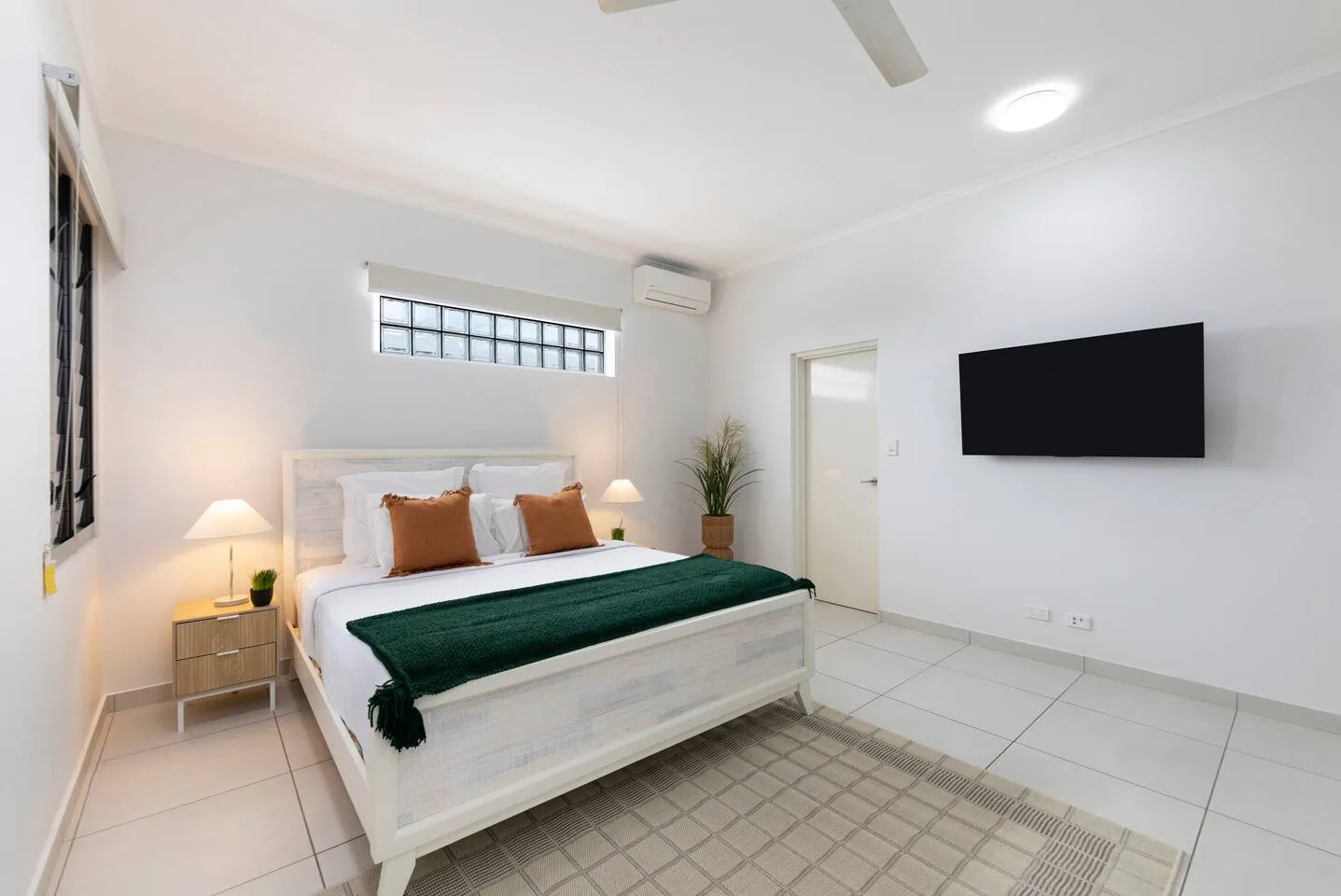 Un dormitorio luminoso con una cama, un televisor en la pared y suelo de baldosas.