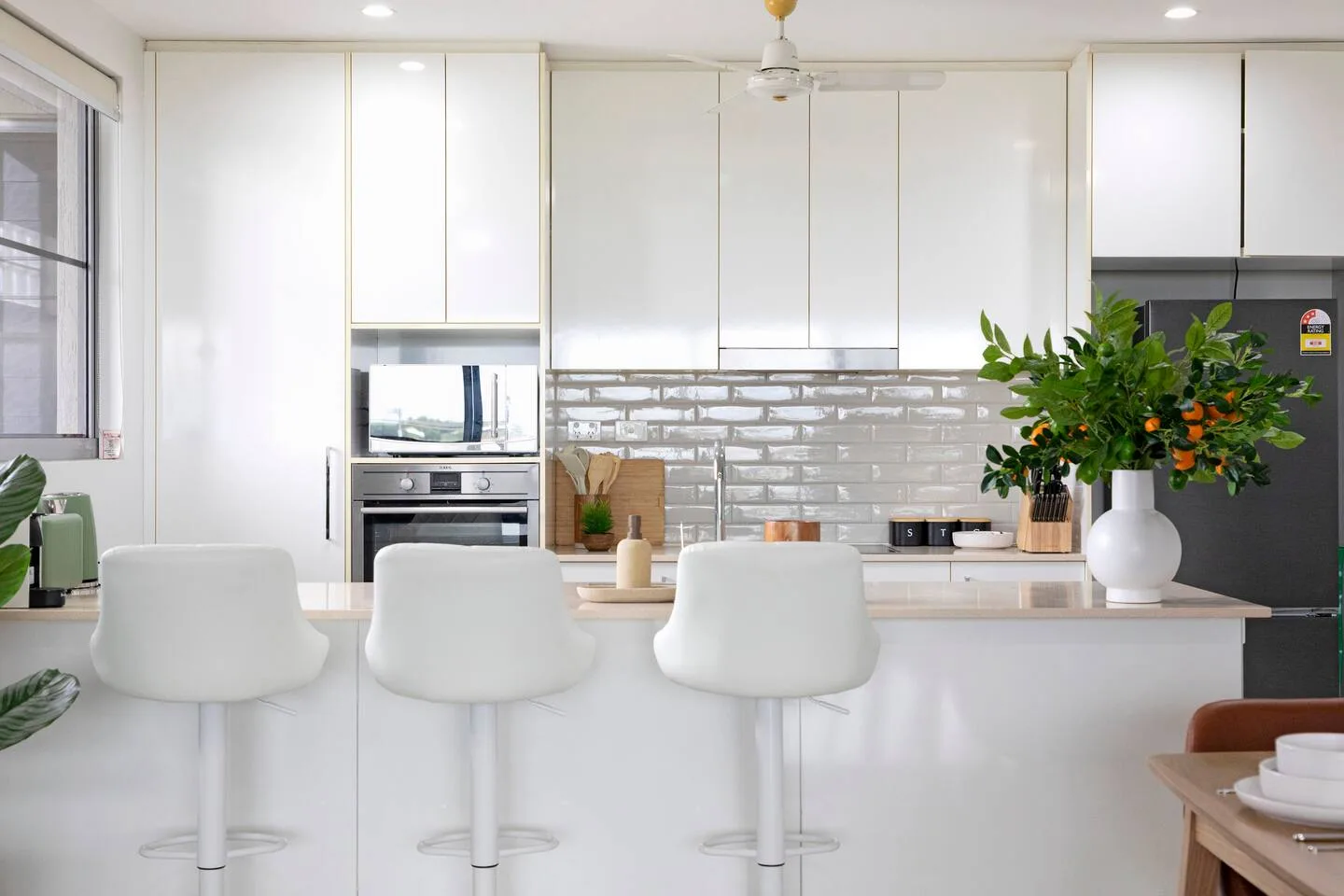 Una cocina luminosa con gabinetes blancos, un salpicadero de azulejos y asientos junto a la encimera.