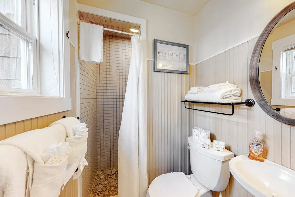 Un baño con ducha, inodoro y lavabo bajo un espejo redondo.