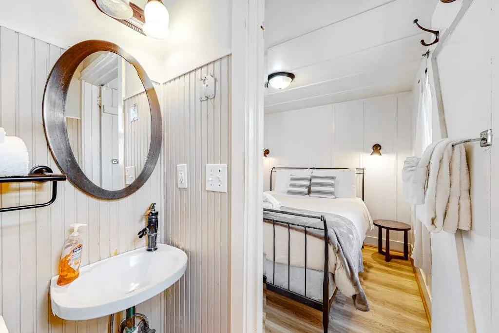 Dormitorio con una cama de estructura metálica y una pequeña zona de lavabo al lado.