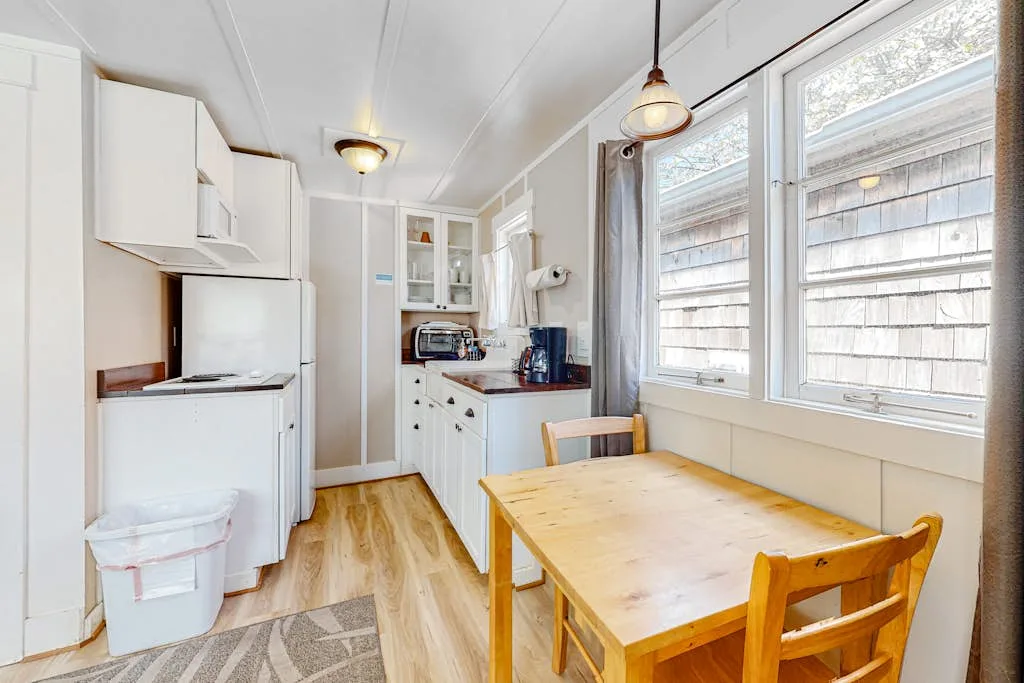 Una luminosa cocina y comedor con una mesa de madera junto a grandes ventanas.