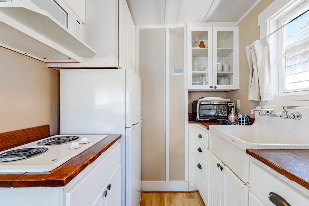 Una cocina compacta con estufa, refrigerador y fregadero bajo una ventana.