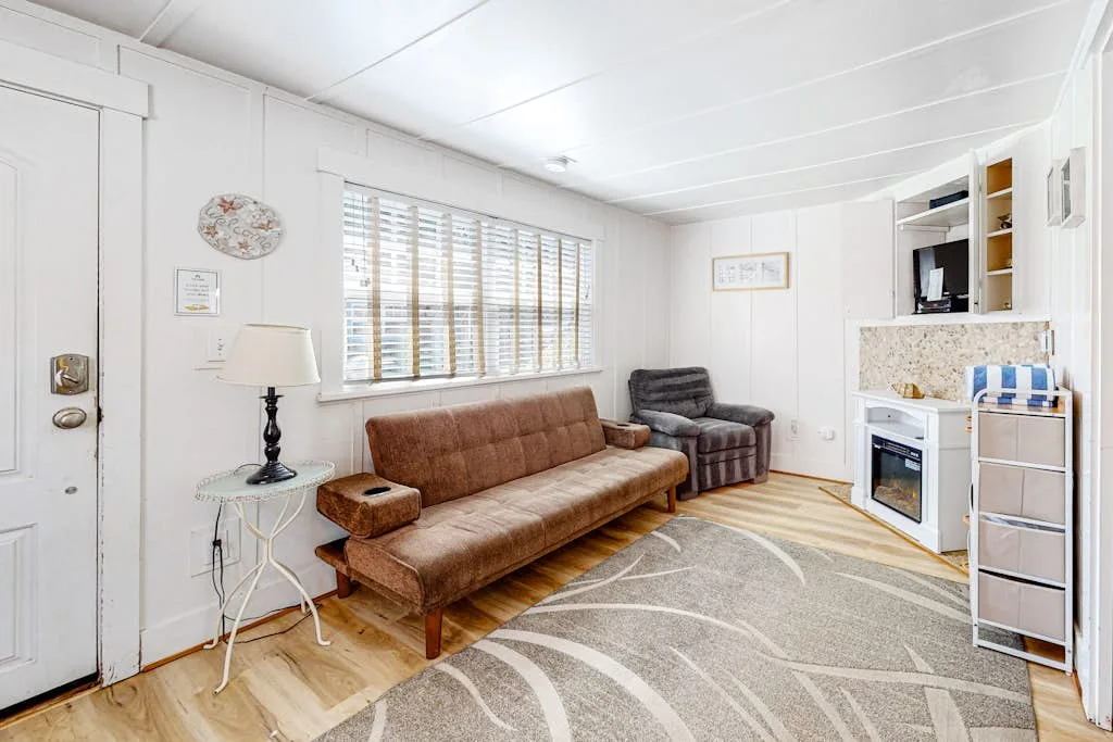 Una sala luminosa con un sofá marrón, un sillón y una alfombra estampada.