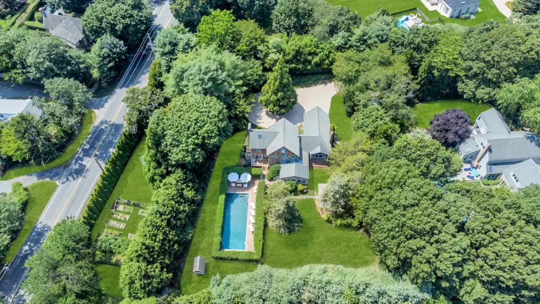 Vista aérea de una casa y su larga piscina exterior, rodeadas de árboles.
