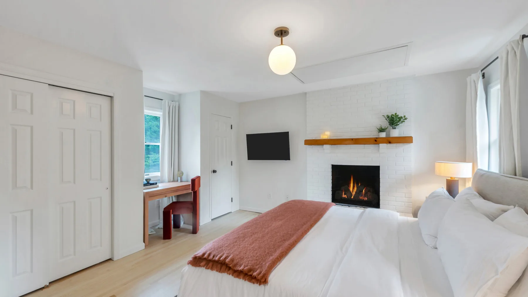 Un dormitorio luminoso con una cama blanca y una chimenea en la pared del fondo.