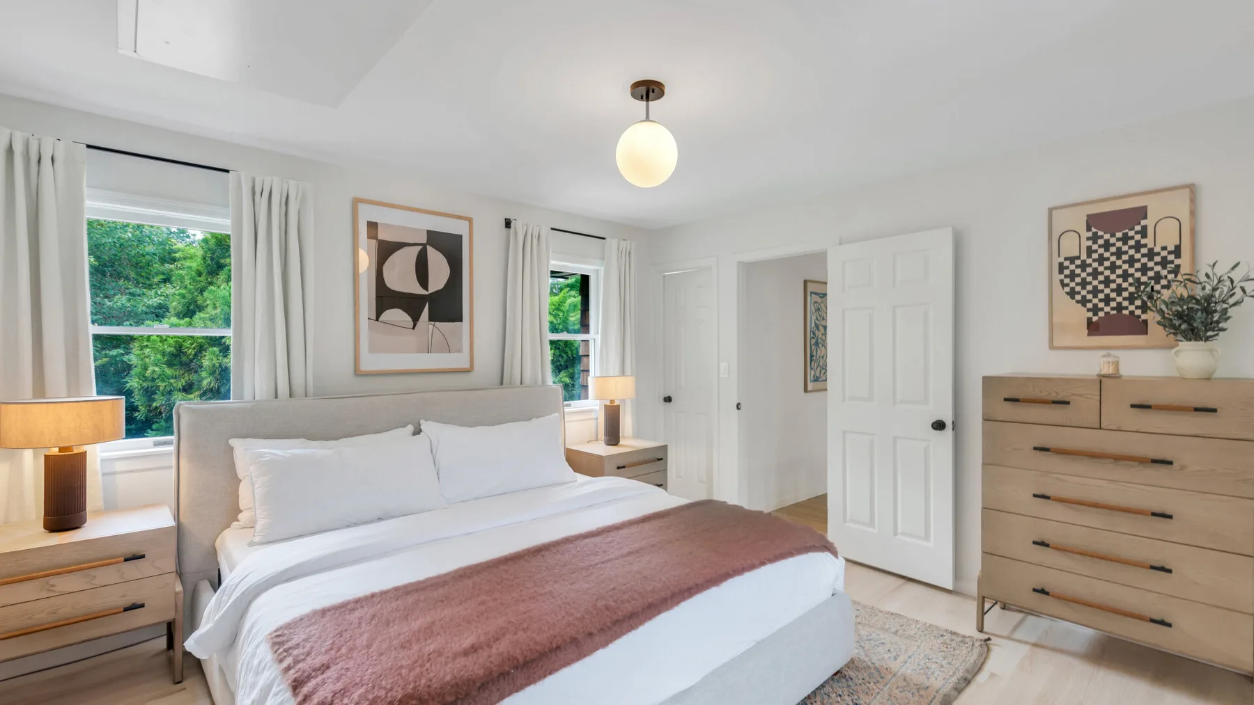 Un dormitorio luminoso con una cama bien tendida y cómodas de madera clara.