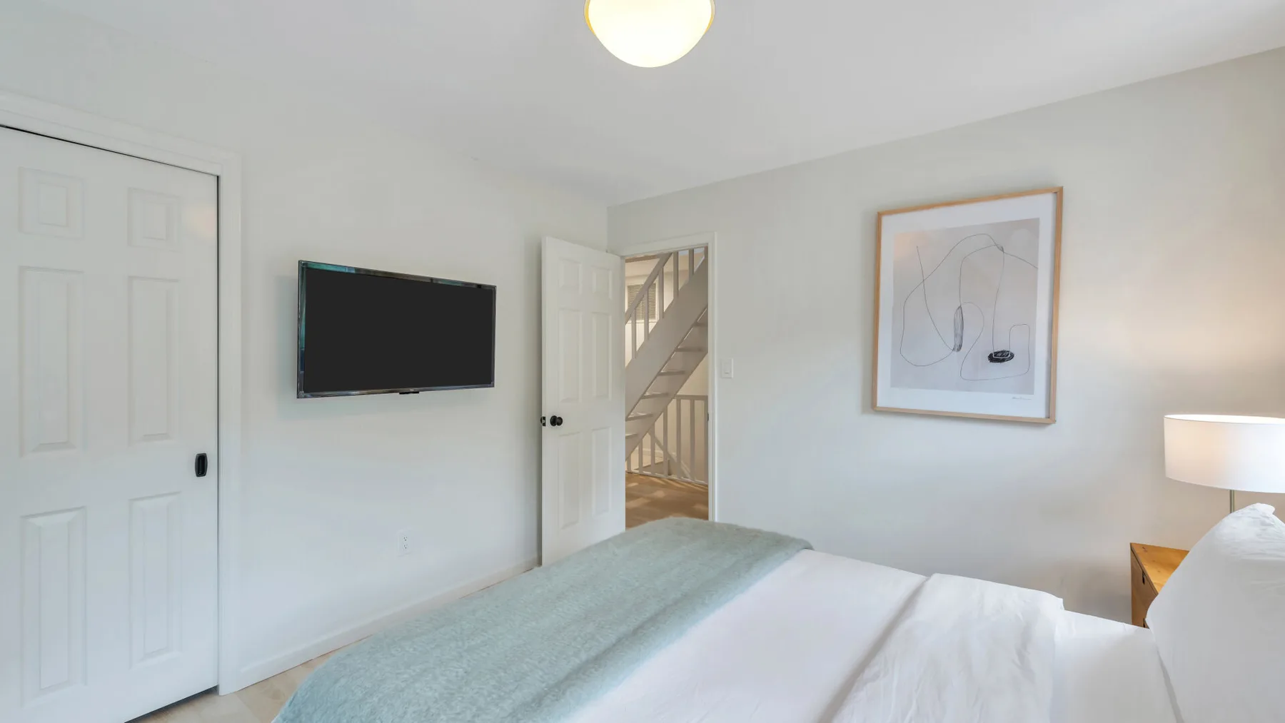 Un dormitorio con una cama, un televisor en la pared y una puerta hacia una escalera.