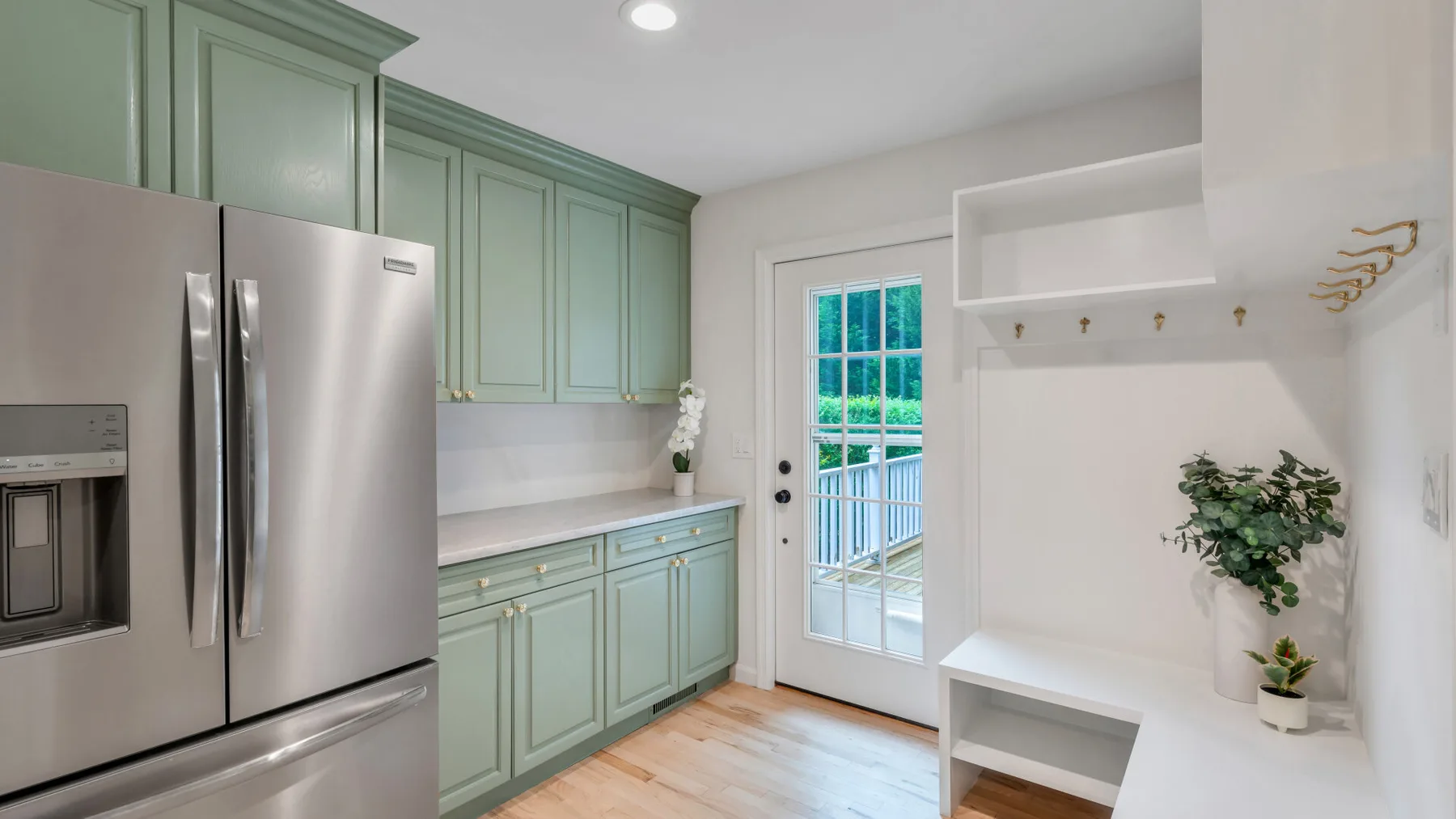 Una cocina luminosa con gabinetes verdes y un refrigerador de acero inoxidable junto a una puerta acristalada.