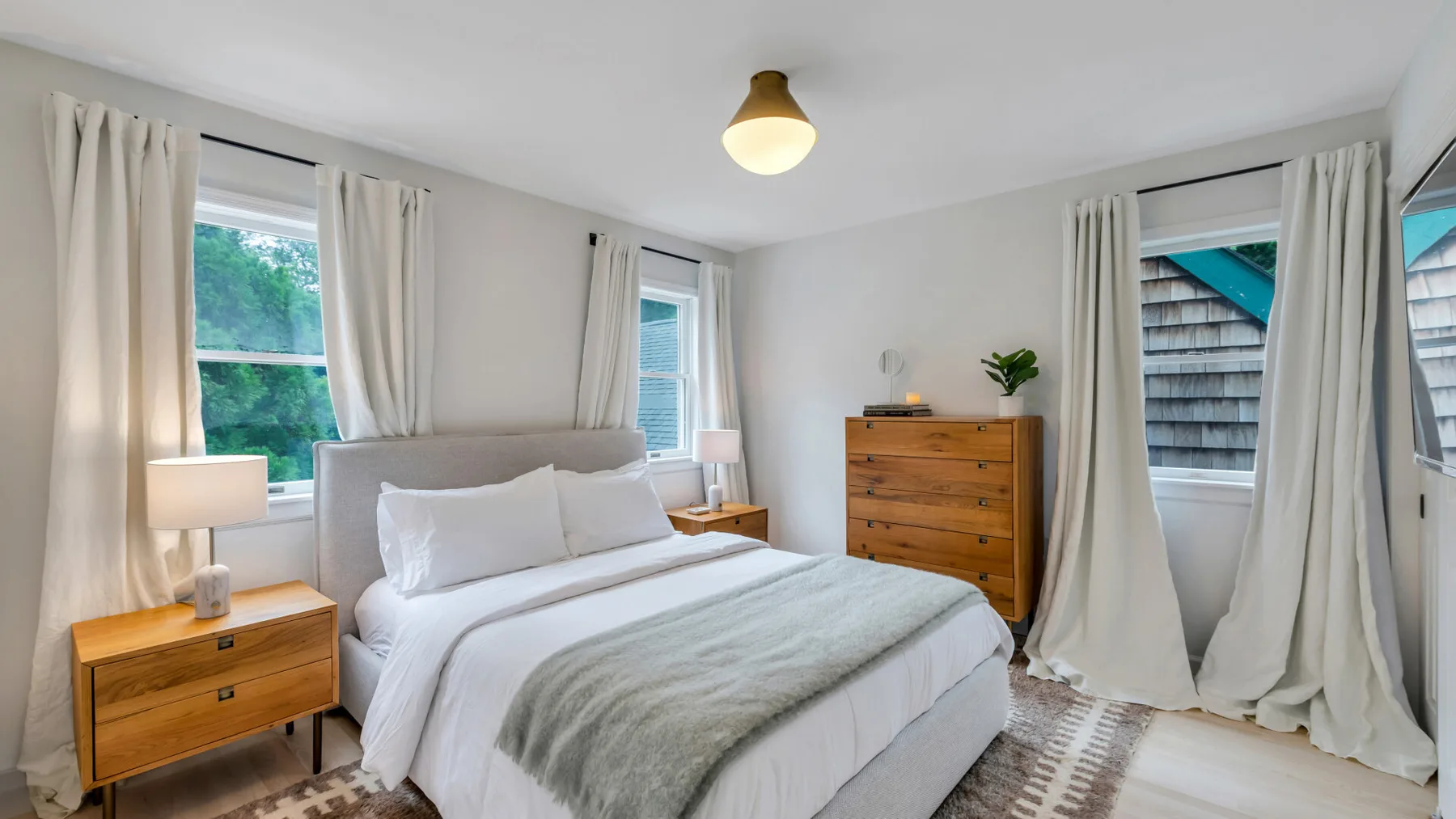 Un dormitorio con una cama, cómodas de madera y ventanas con cortinas.