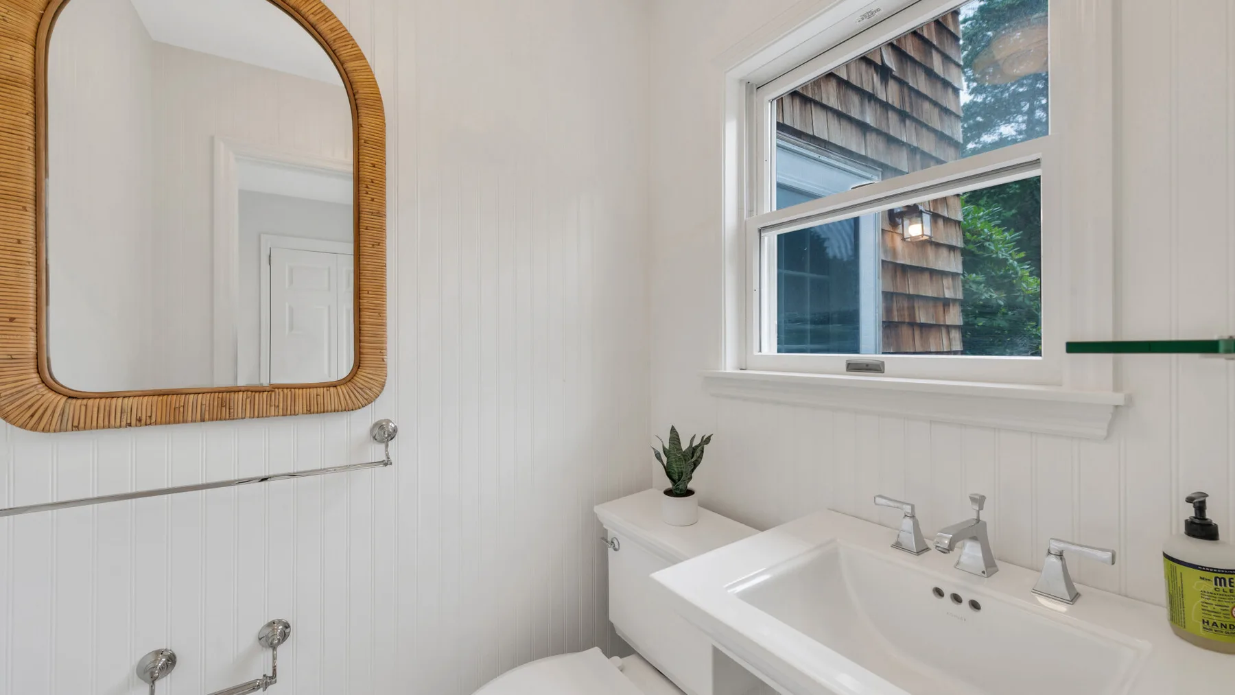 Un baño con lavabo blanco, espejo de pared y ventana.