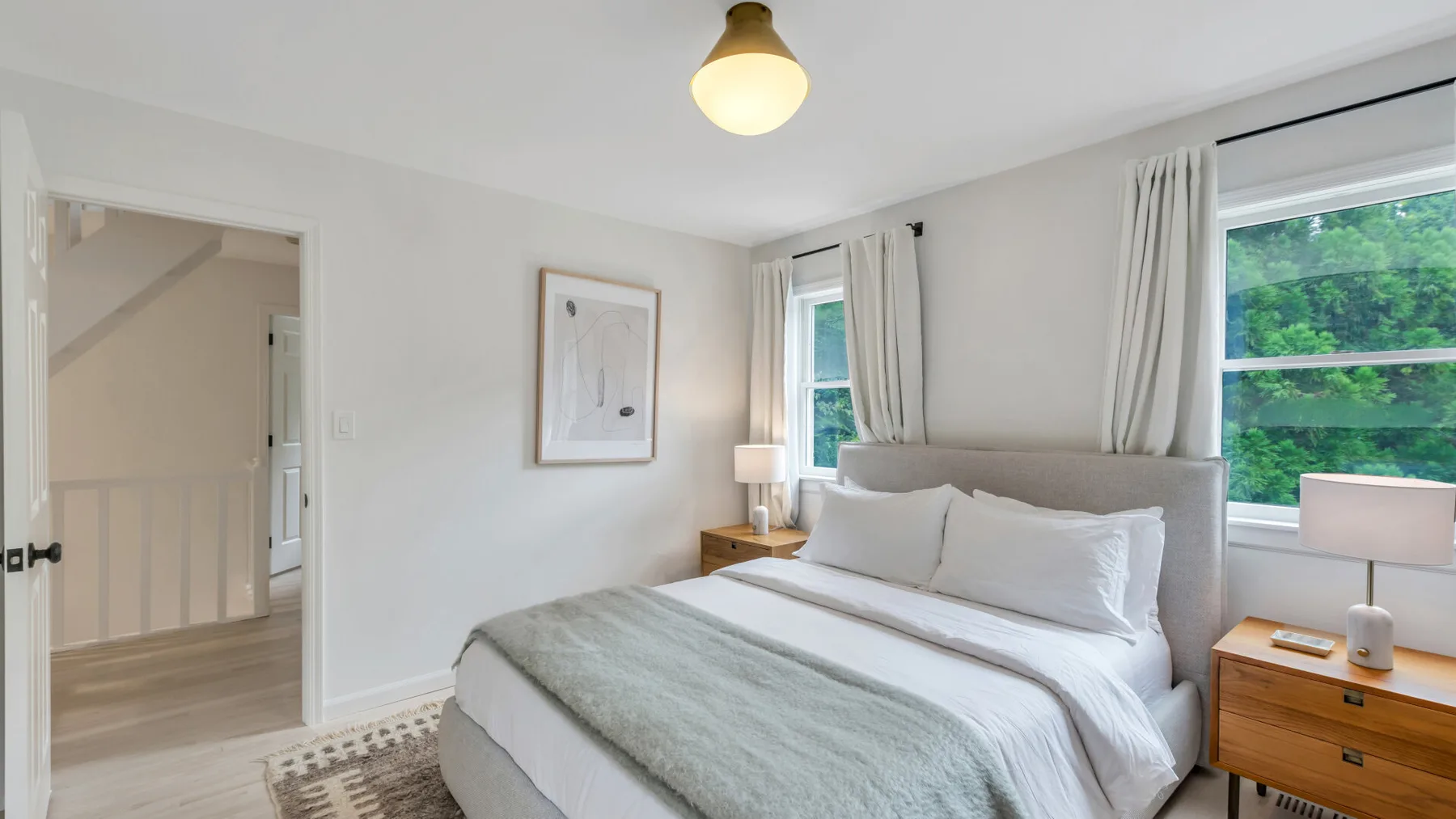 Un dormitorio luminoso con una cama bien tendida y ventanas con vistas a la vegetación.