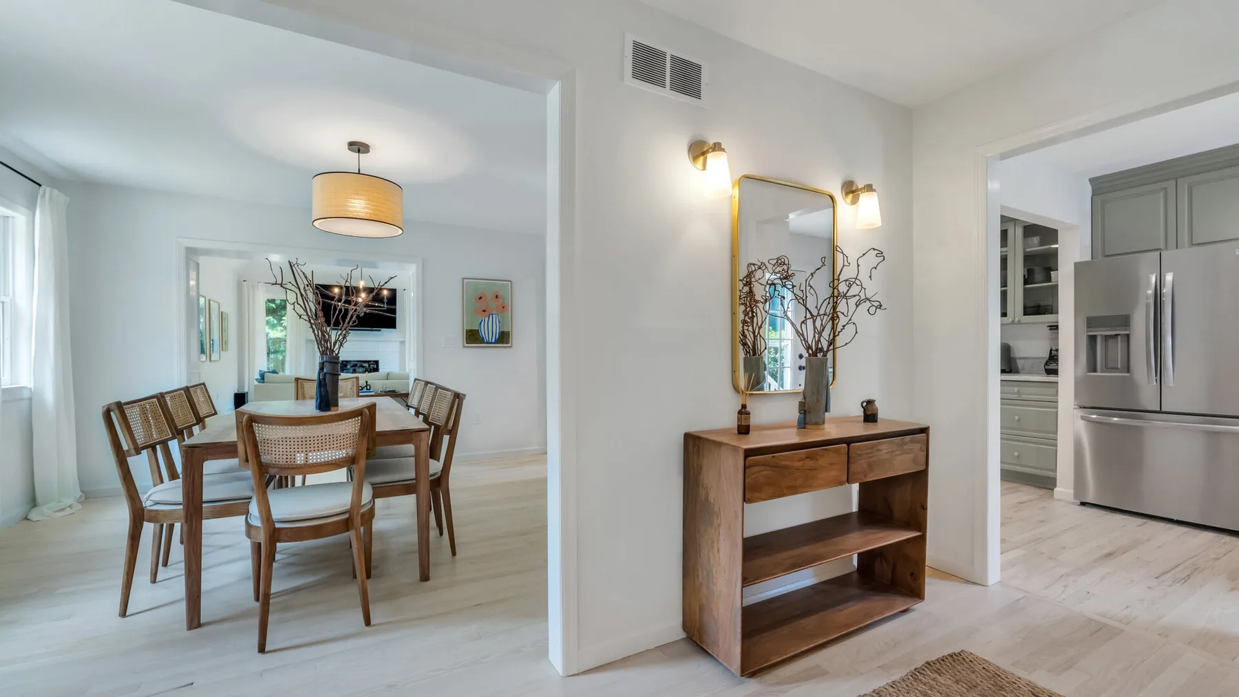 Un comedor luminoso con una mesa de madera y una consola bajo un espejo.