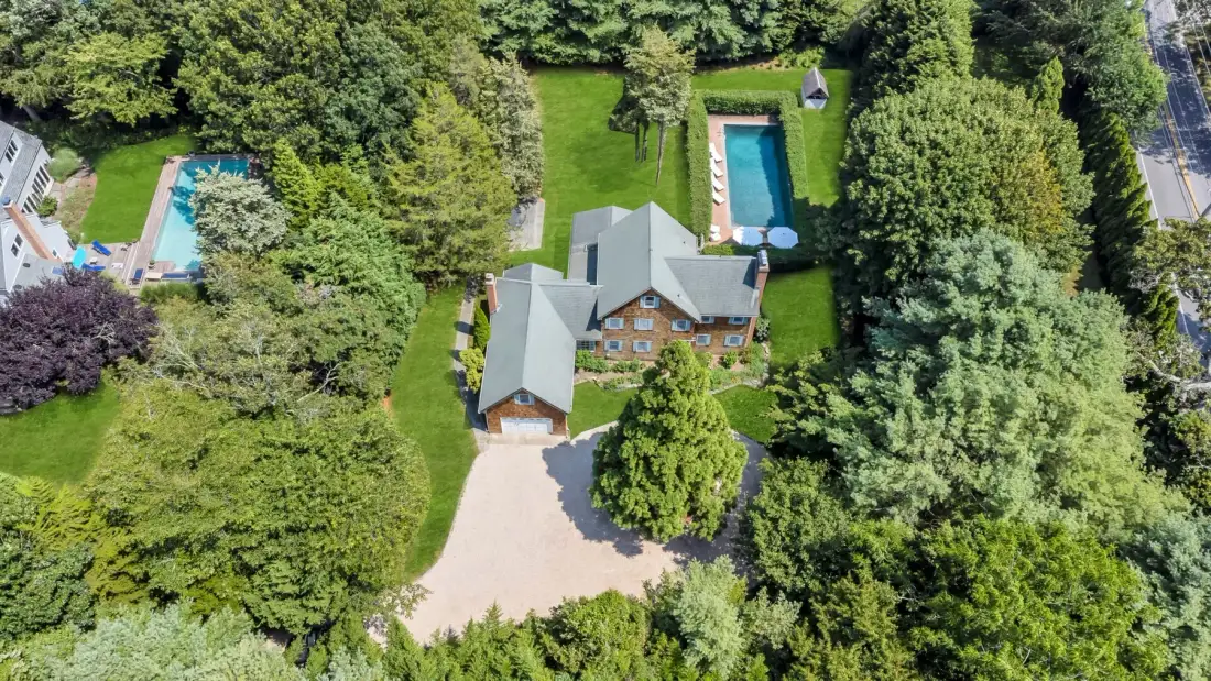 Vista aérea de una casa entre árboles, con entrada para vehículos y piscina al aire libre.
