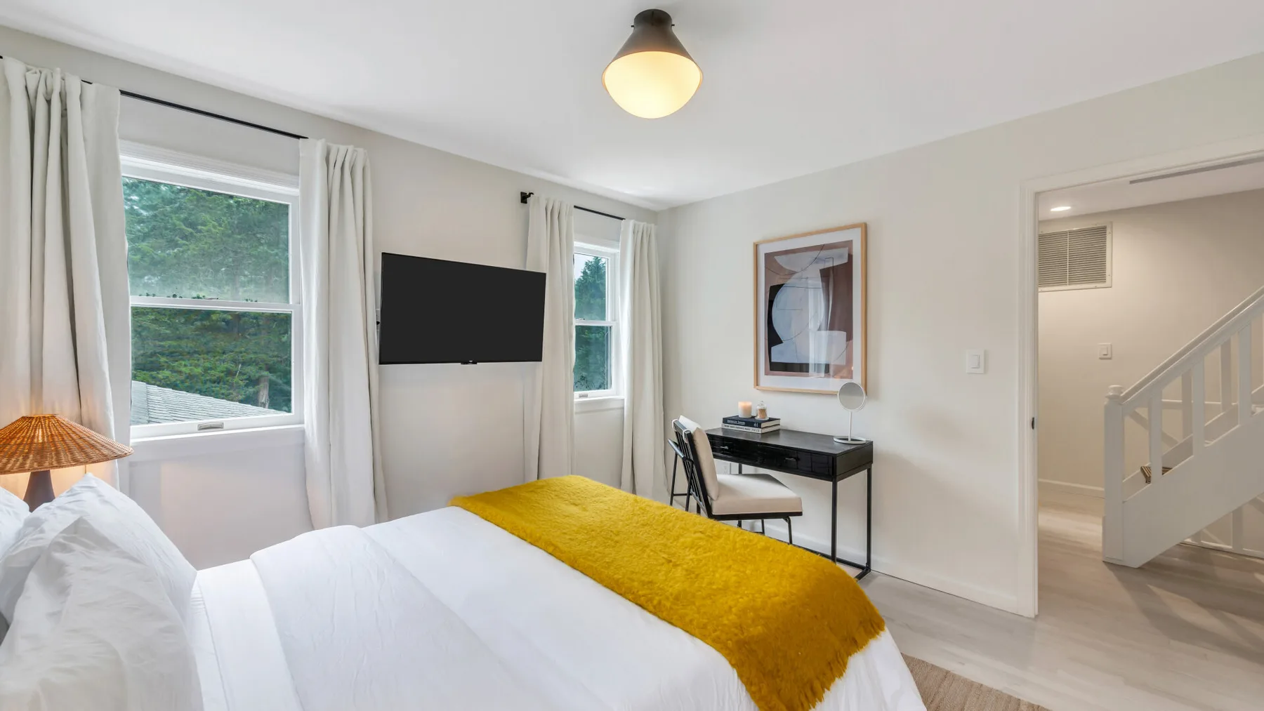 Un dormitorio con una cama blanca, una manta mostaza y un televisor en la pared.