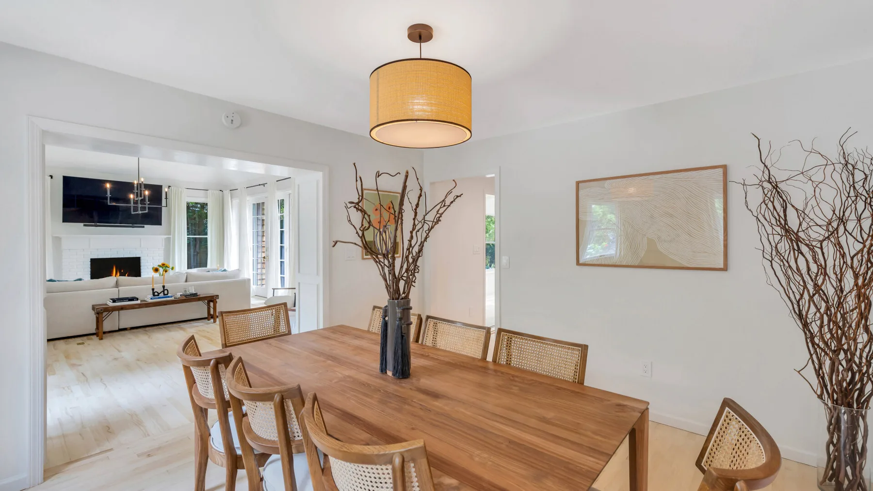Comedor con una mesa de madera y sillas tejidas bajo una lámpara colgante.