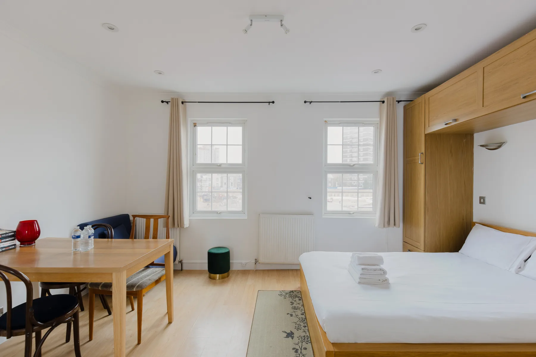 A bright bedroom with a bed, a desk, and two windows.