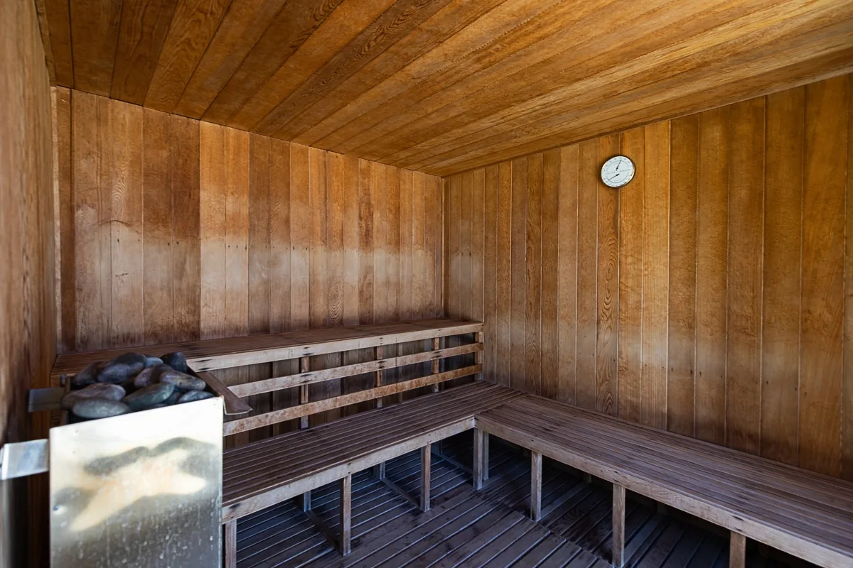Una sauna revestida de madera tiene bancos escalonados y un reloj en la pared.
