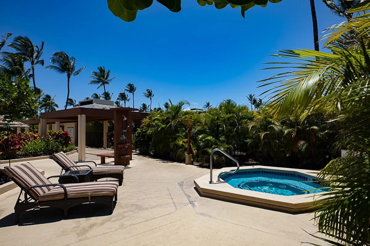 Una piscina exterior y un patio con asientos entre vegetación tropical.