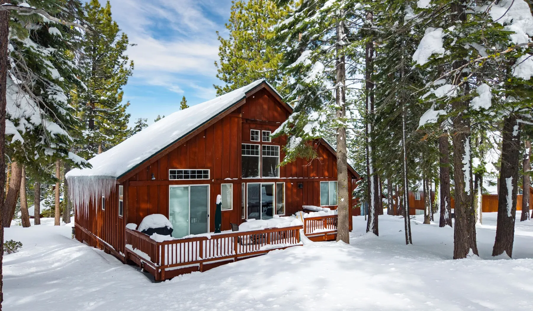 Una cabaña roja con una terraza de madera se encuentra entre árboles cubiertos de nieve.