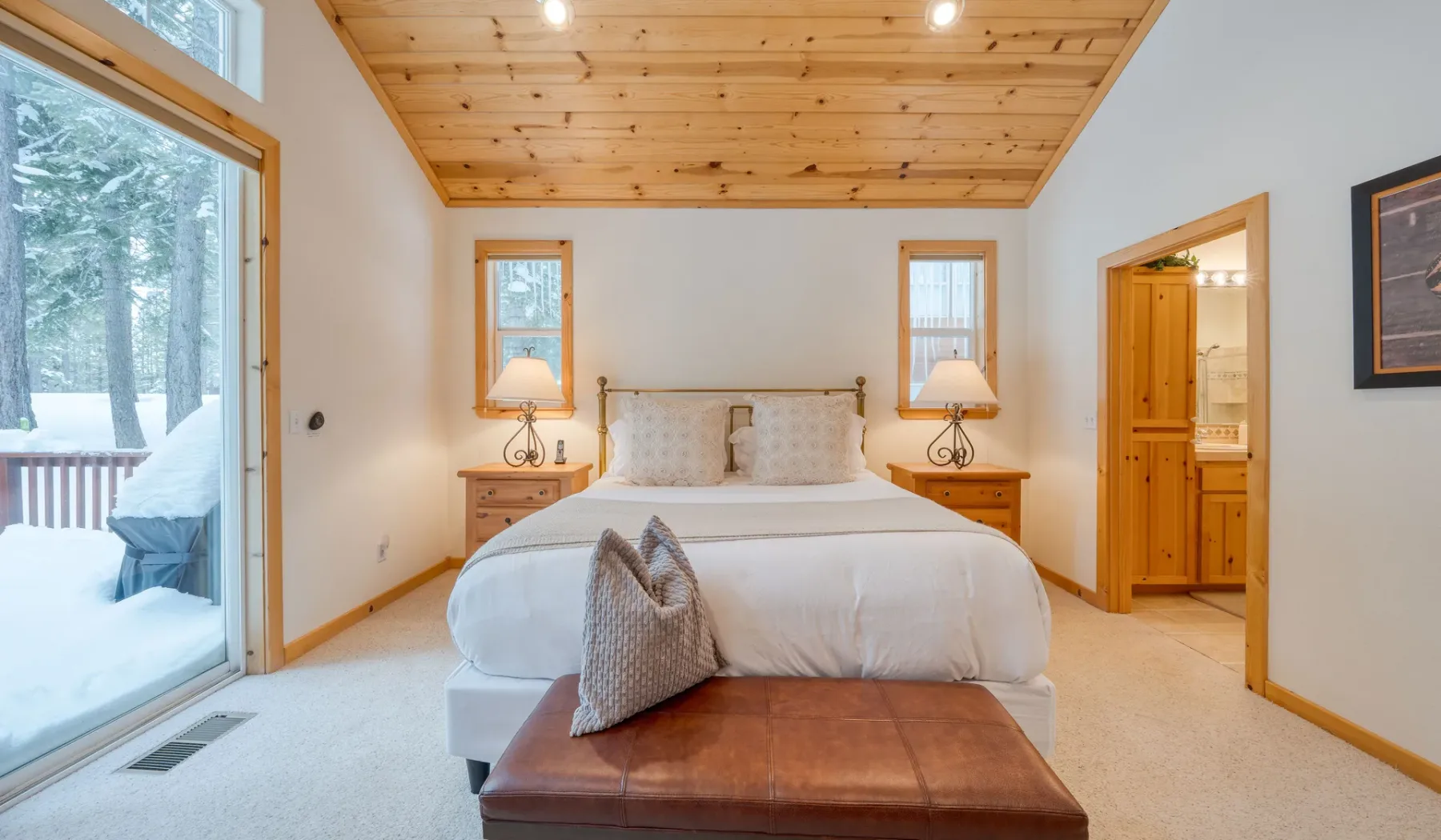 Un dormitorio con una cama bajo un techo revestido de madera y una puerta de vidrio hacia un paisaje nevado.