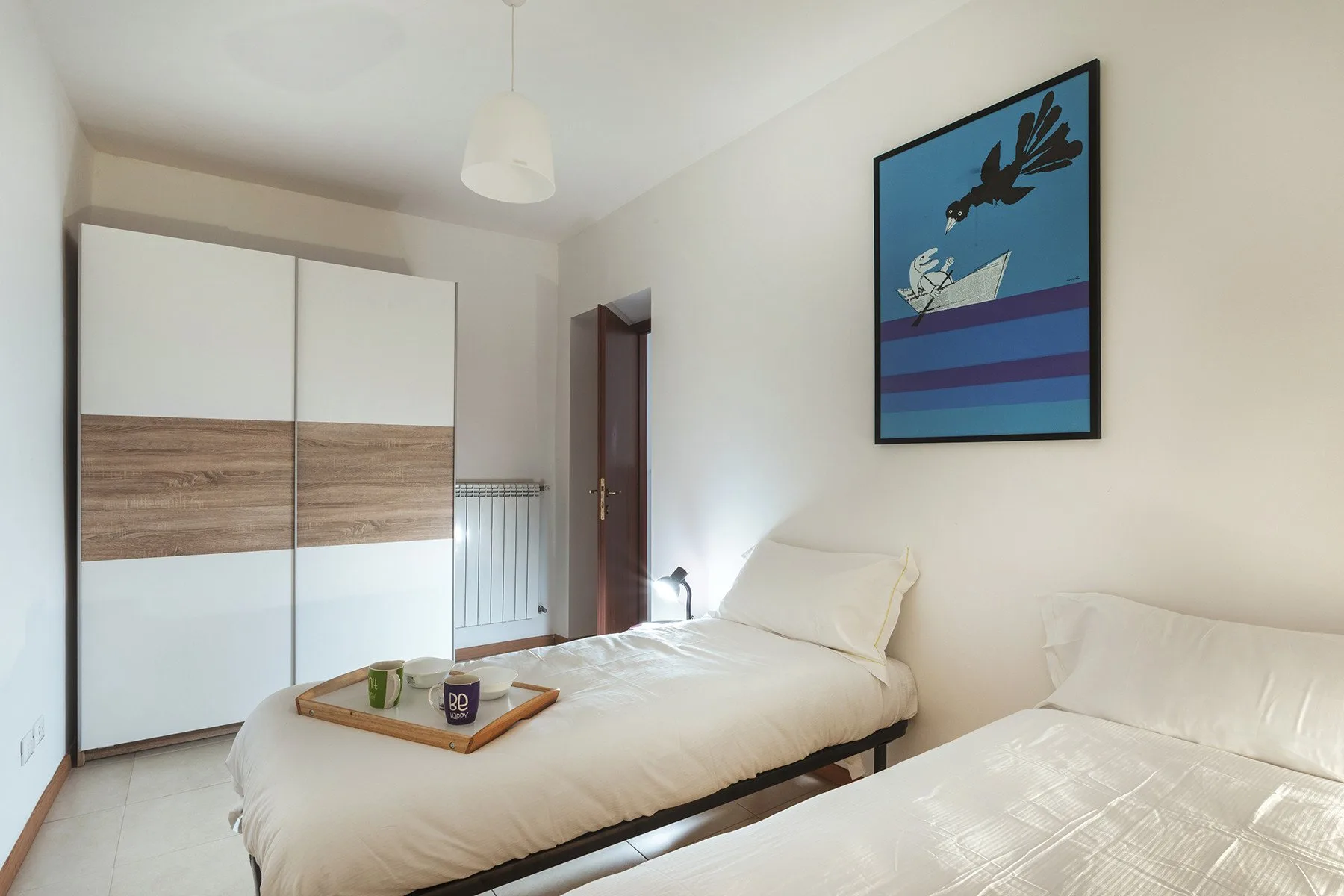 Un dormitorio luminoso con ropa de cama blanca, un armario y arte colorido en la pared.