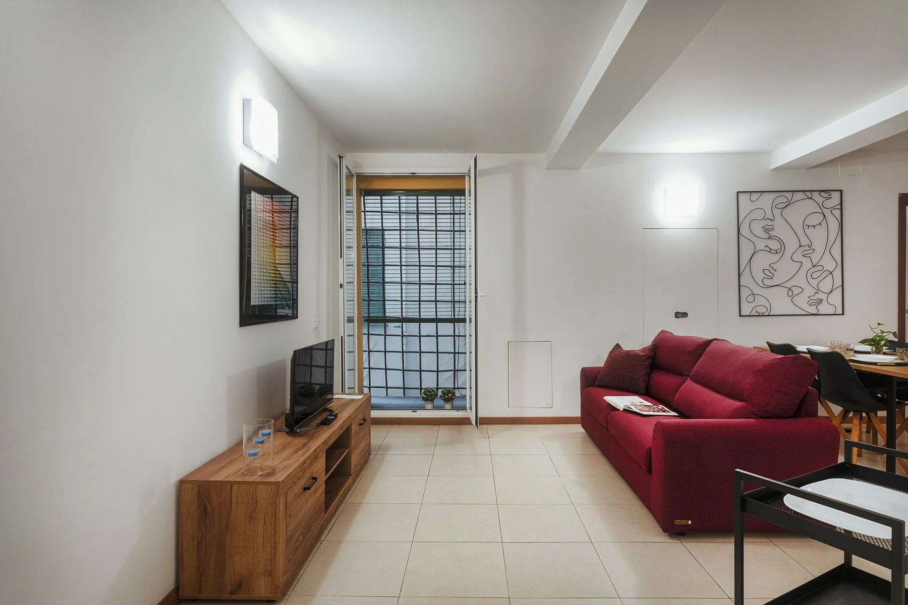 Una sala de estar con asientos rojos, un televisor y una ventana grande.