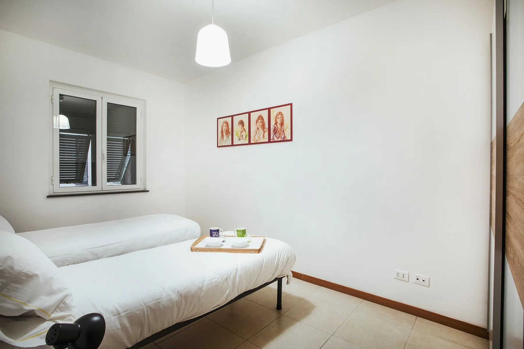 Un dormitorio luminoso con una cama blanca, una ventana y cuadros enmarcados.