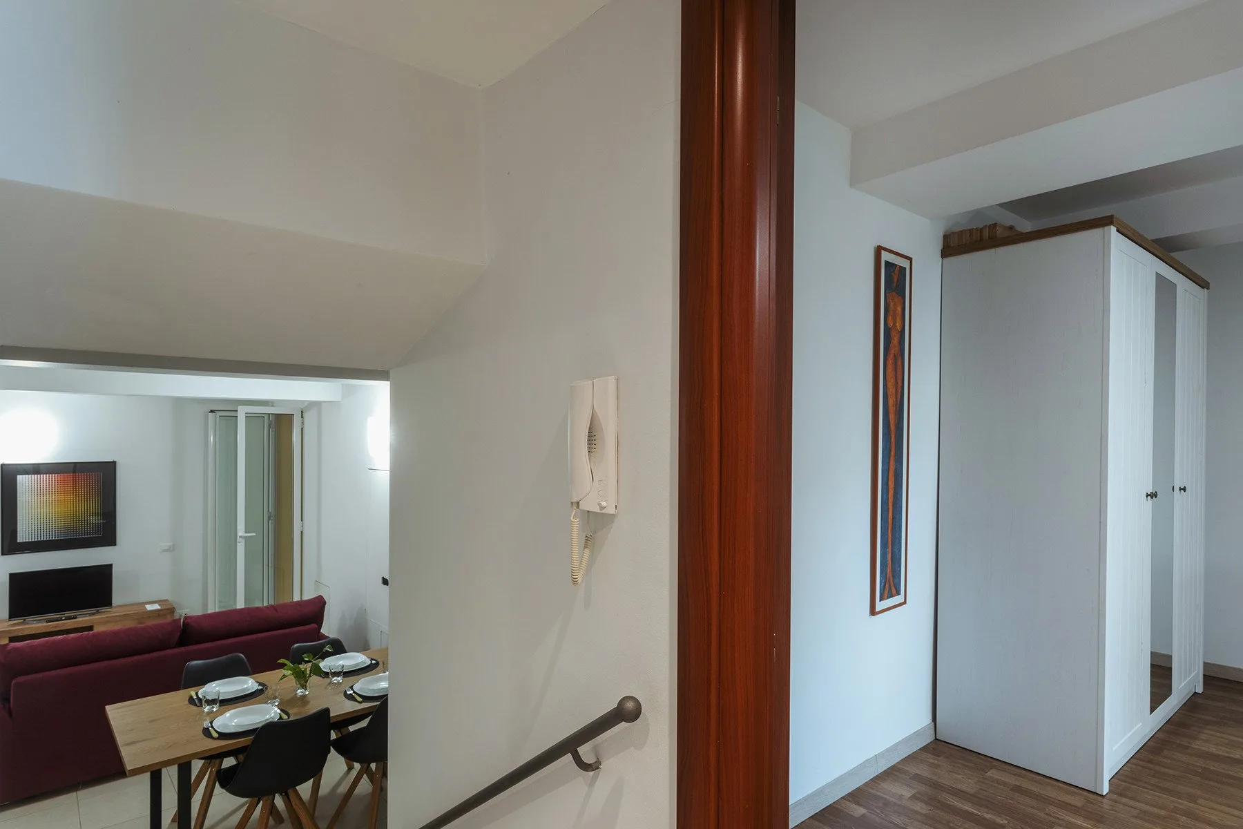 Un interior a distinto nivel muestra un comedor y una sala junto a un armario blanco alto.