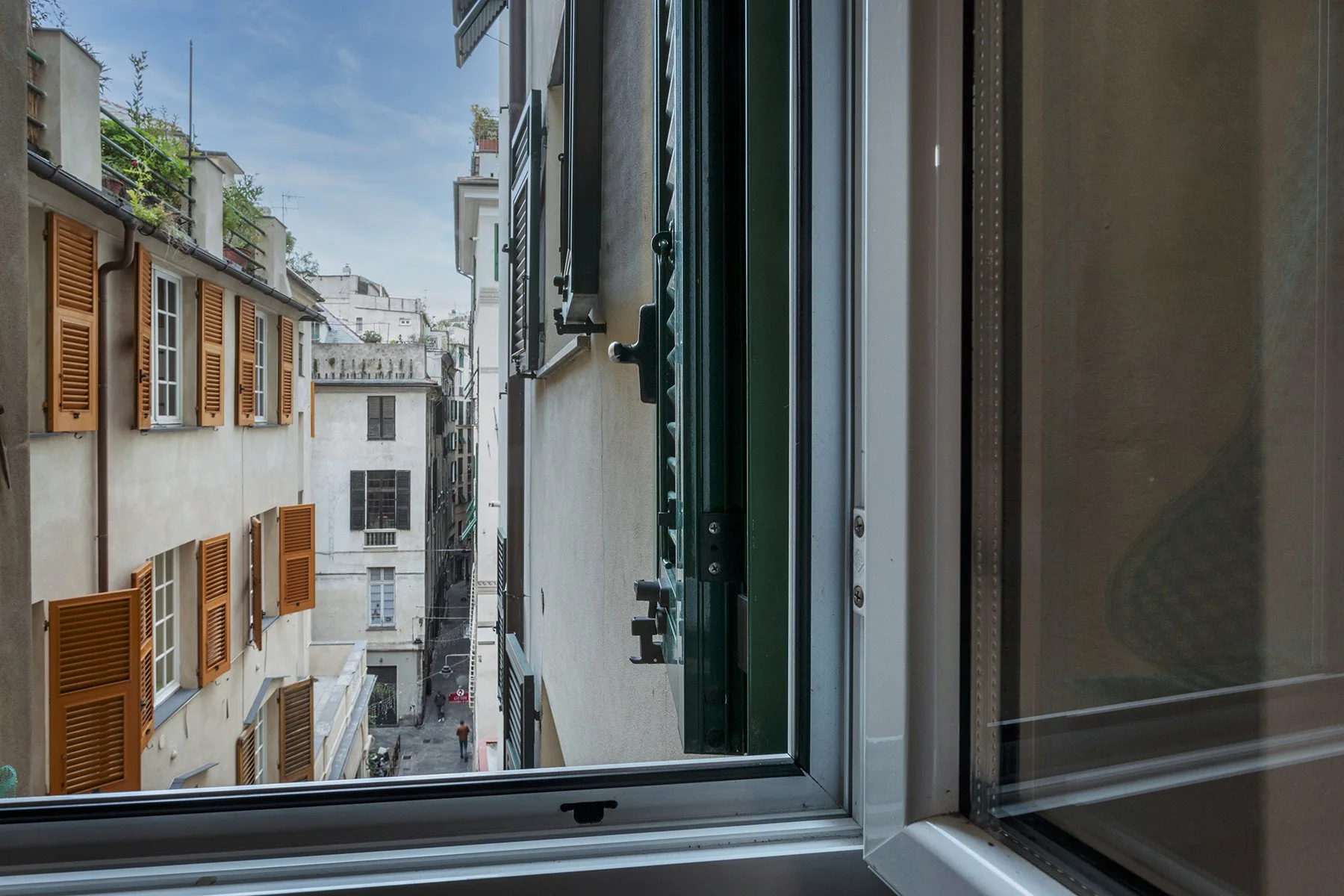 Vista de una calle urbana estrecha y fachadas cercanas a través de una ventana abierta.