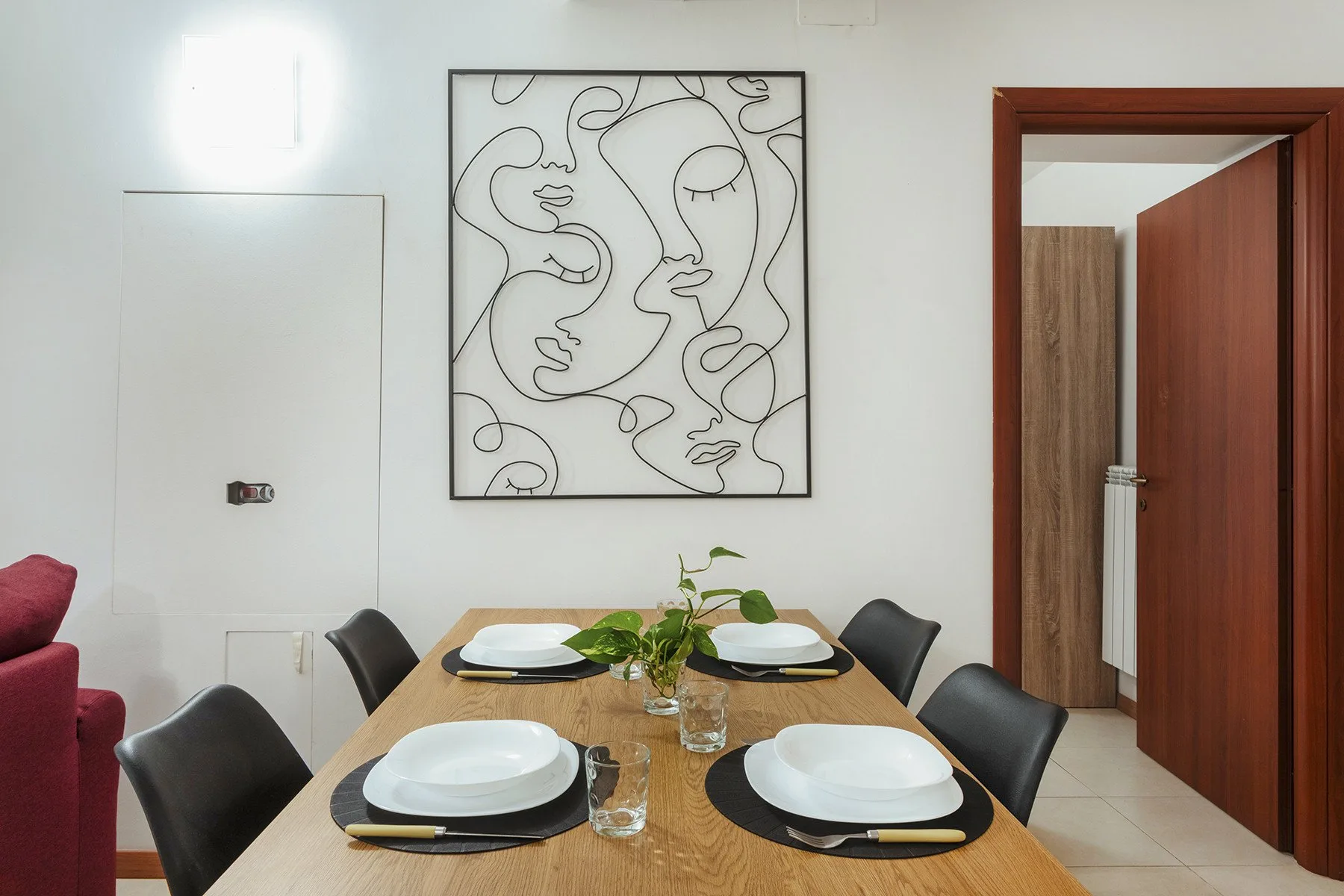 Comedor con una mesa de madera puesta con platos bajo un cuadro de arte lineal.