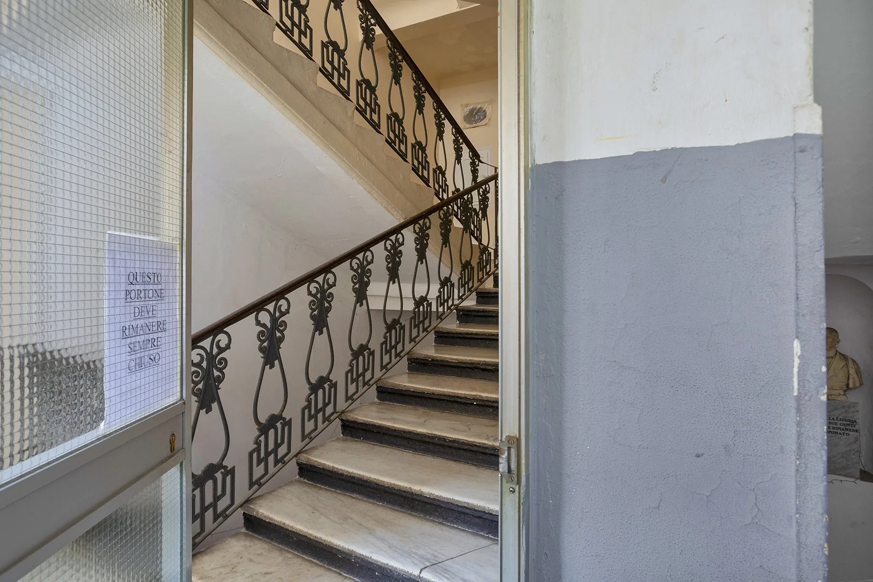 Una escalera interior con peldaños de baldosas y barandillas de metal ornamentadas.