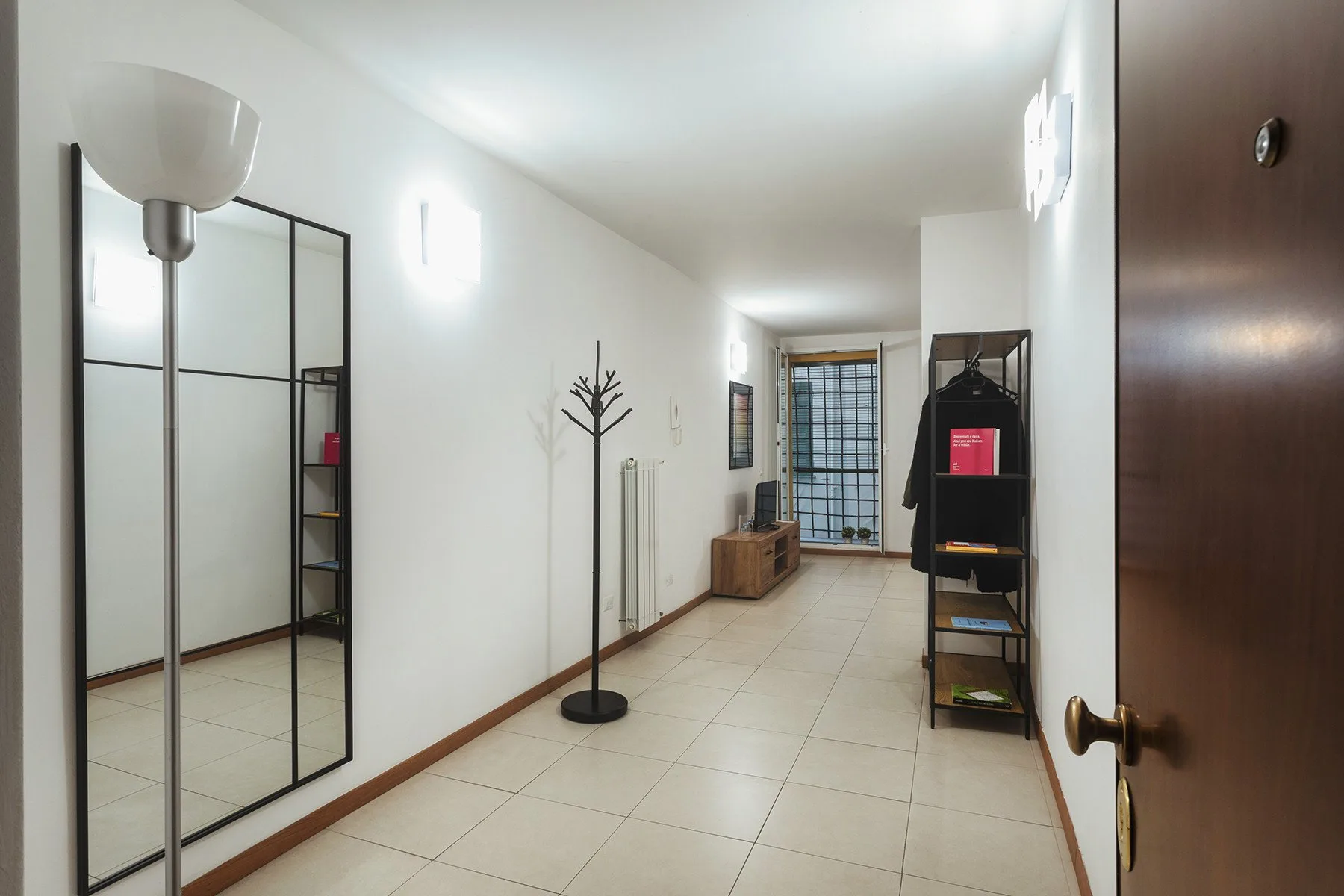 A bright tiled hallway with a coat rack and storage shelves.