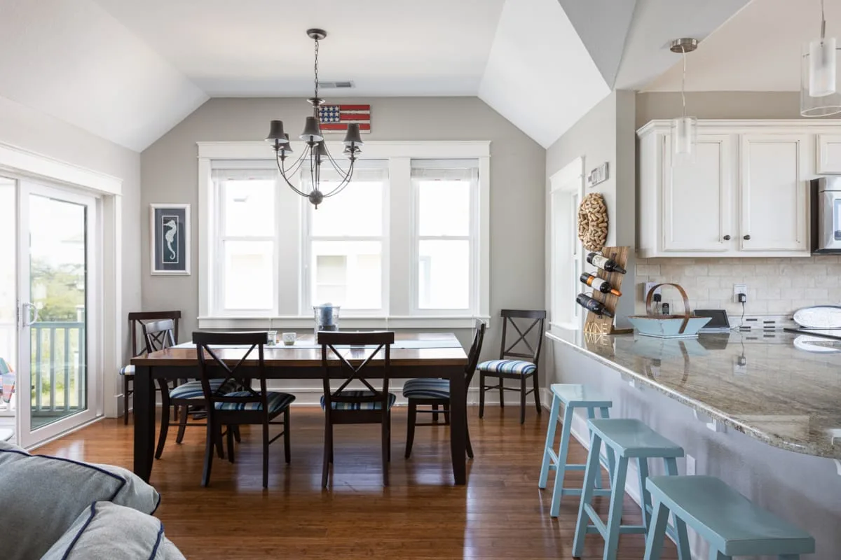 Comedor con una mesa oscura y sillas junto a una cocina luminosa.