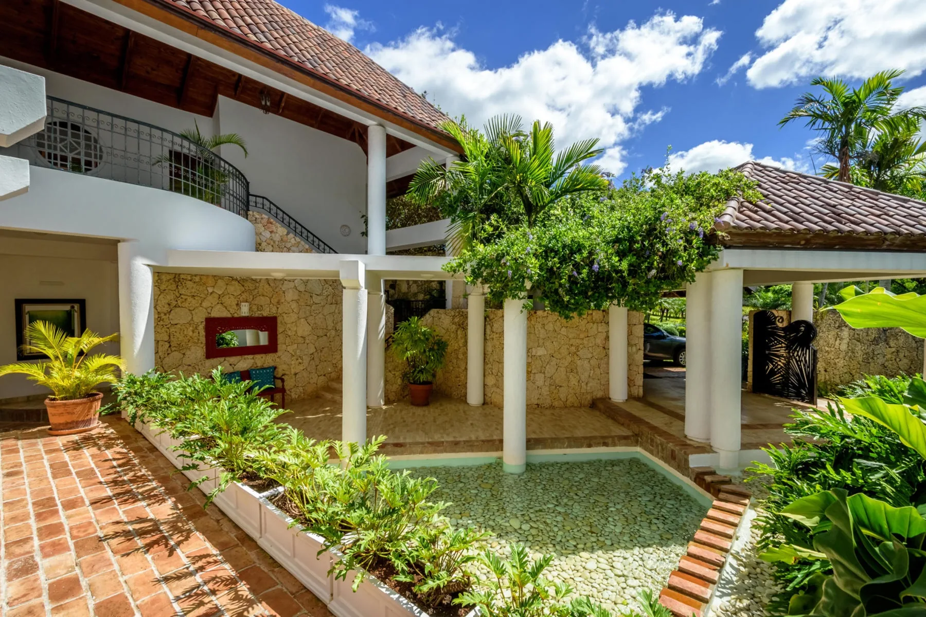 Un patio tropical con una piscina poco profunda, muros de piedra y plantas frondosas.