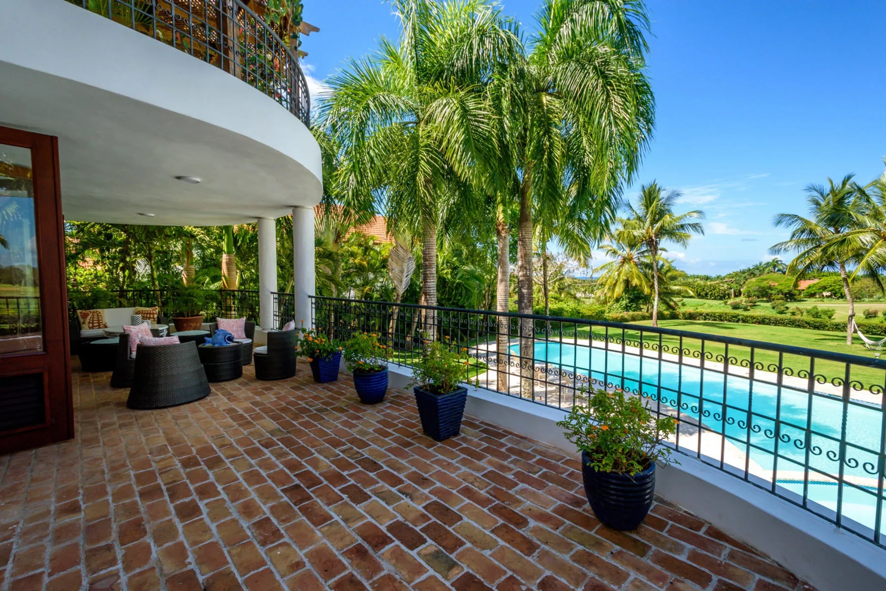 Un patio de baldosas con asientos al aire libre da a una piscina y palmeras.