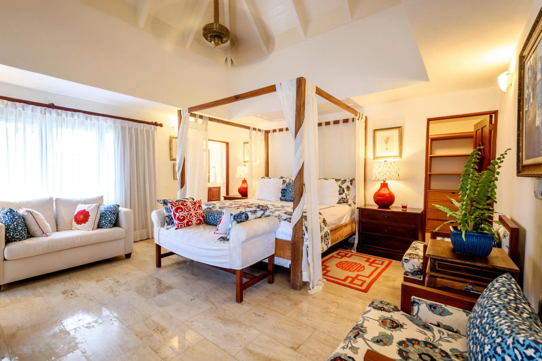 Un dormitorio con cama con dosel, asientos y una gran ventana con cortinas.