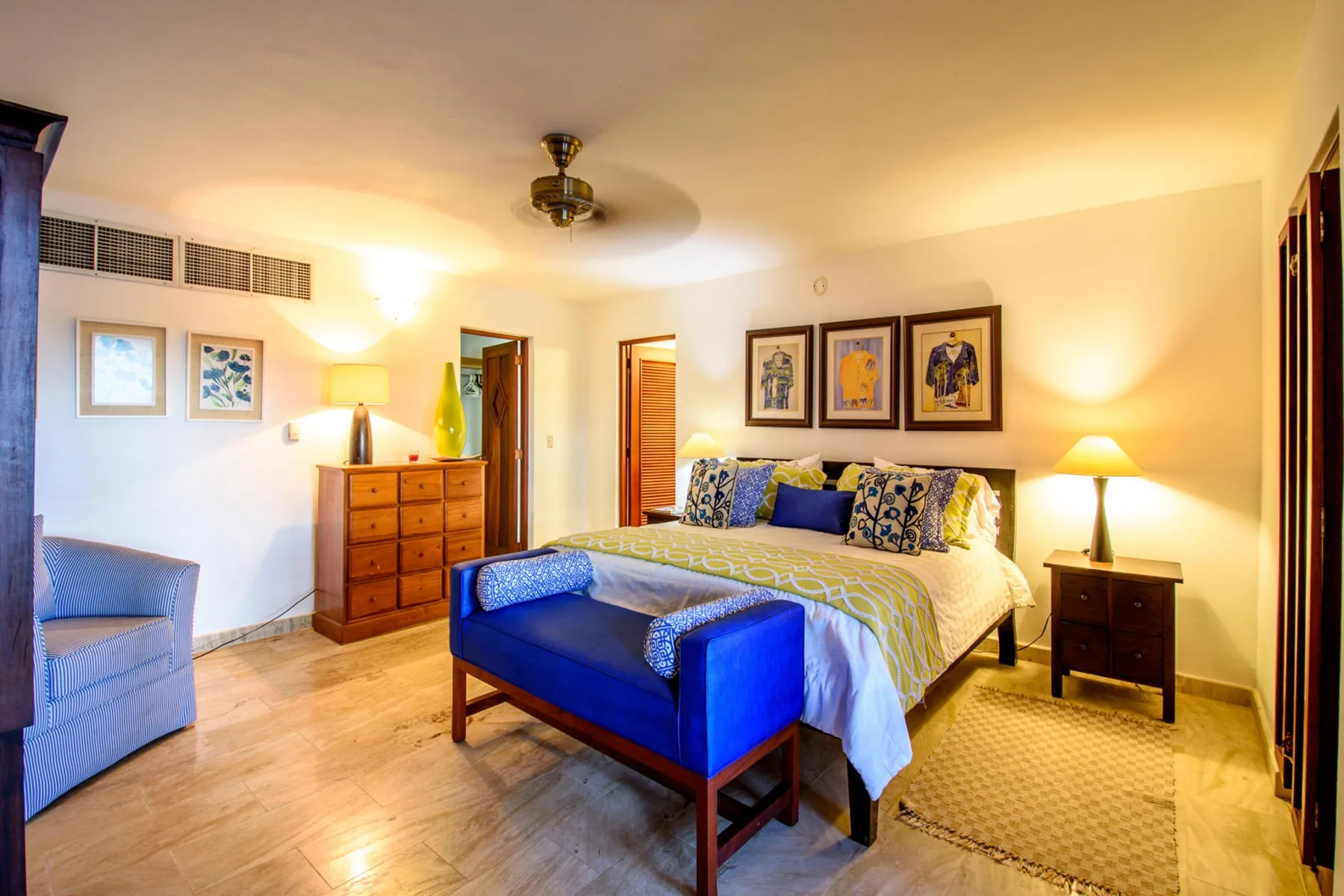 Un dormitorio con una cama azul, una cómoda de madera y cuadros enmarcados.