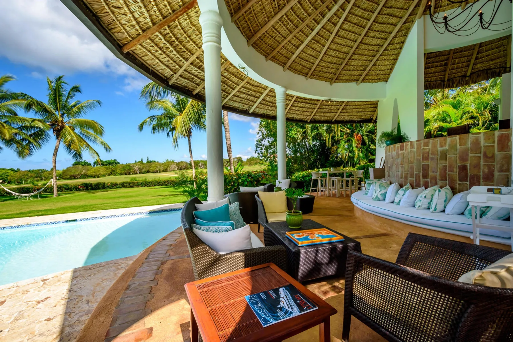 Una sala al aire libre tiene vistas a una piscina y vegetación tropical.