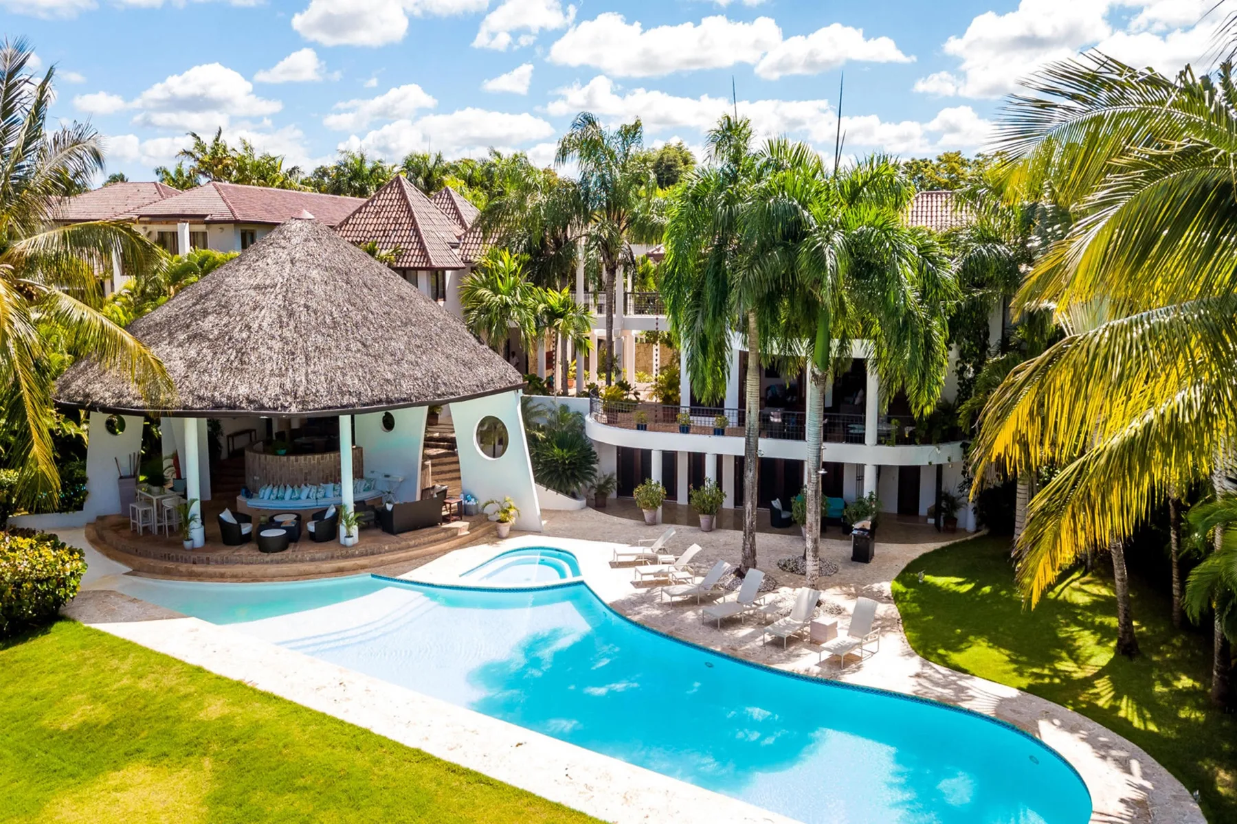 Una zona de piscina tropical con un pabellón de techo de paja y asientos.