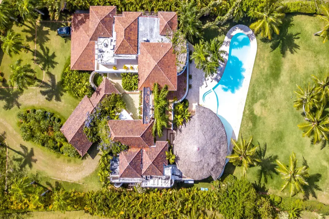 Una vista aérea muestra una propiedad ajardinada con edificios de tejas rojas y una piscina.