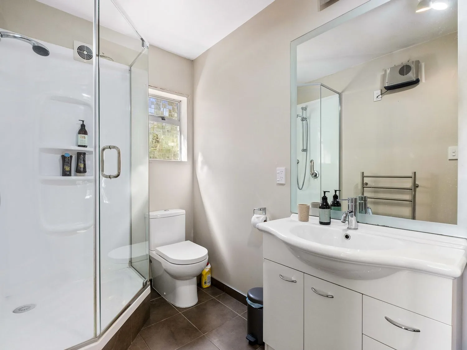Un baño luminoso con ducha, inodoro y lavabo bajo un espejo grande.