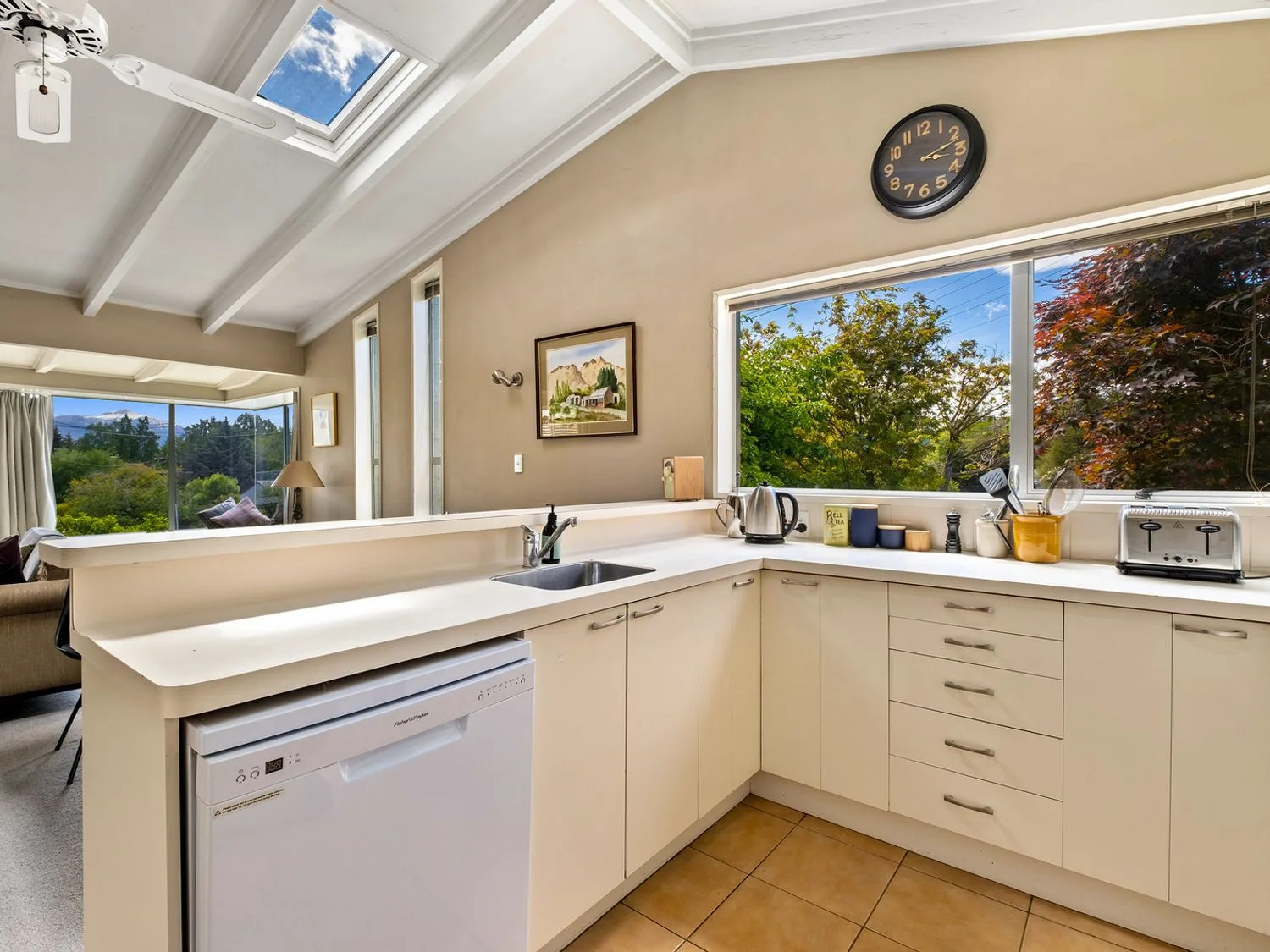 Una cocina con armarios blancos y encimeras, con vistas a los árboles a través de una ventana en Taha Wai - Wanaka Holiday Home, en Wanaka.