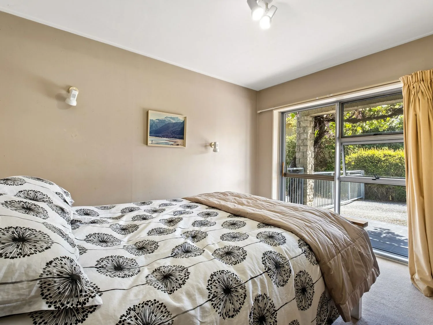 Un dormitorio con ropa de cama estampada junto a una ventana grande con cortinas beige.