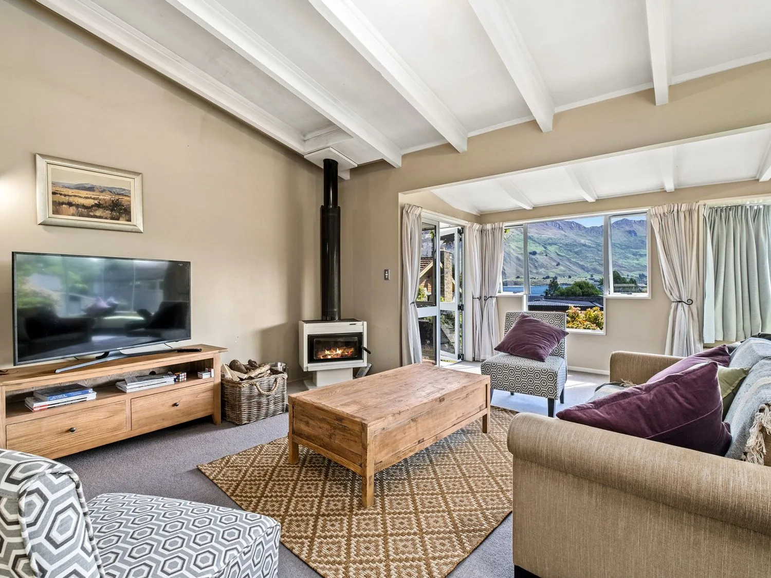 Una sala de estar con un televisor, una estufa de leña y vistas a las montañas por las ventanas.