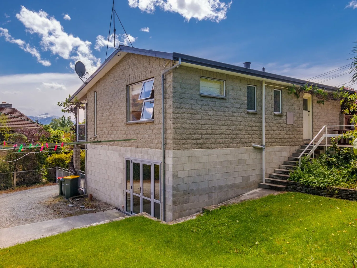Una casa de piedra con escaleras que conducen a una puerta y un jardín con césped en Taha Wai - Wanaka Holiday Home, en Wanaka.