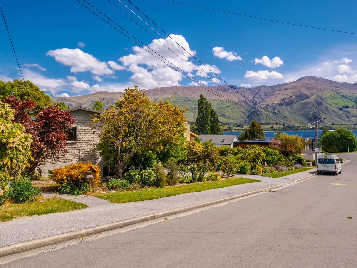Una calle con casas y árboles, con montañas y un lago al fondo, en Taha Wai - Wanaka Holiday Home, en Wanaka.