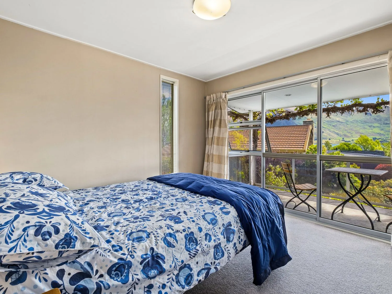 Un dormitorio con ropa de cama floral azul junto a puertas corredizas de vidrio que dan a un balcón.