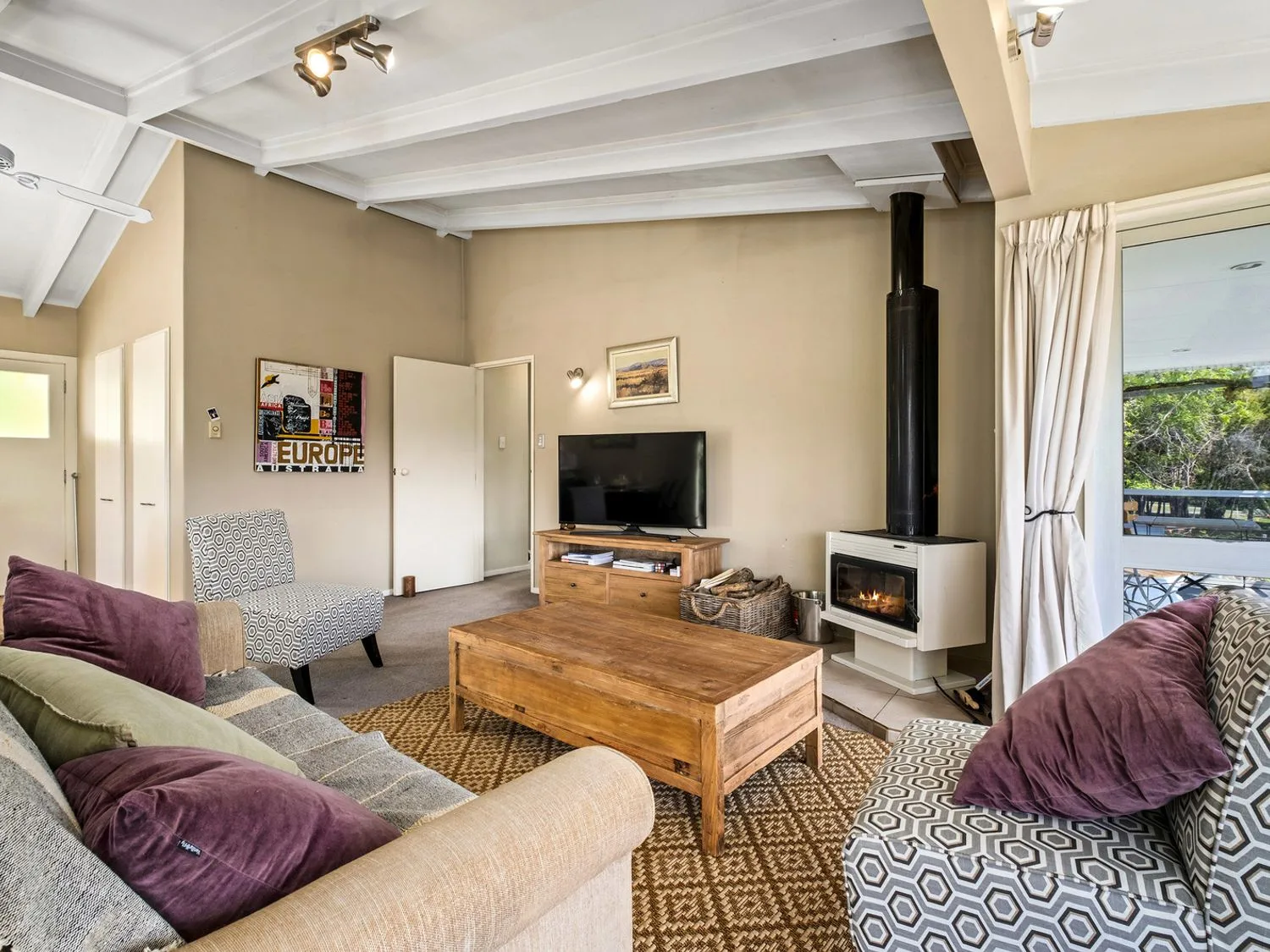 Una sala de estar con una mesa de centro de madera, un televisor sobre un mueble de madera, una chimenea y sillones estampados en Taha Wai - Wanaka Holiday Home, en Wanaka.